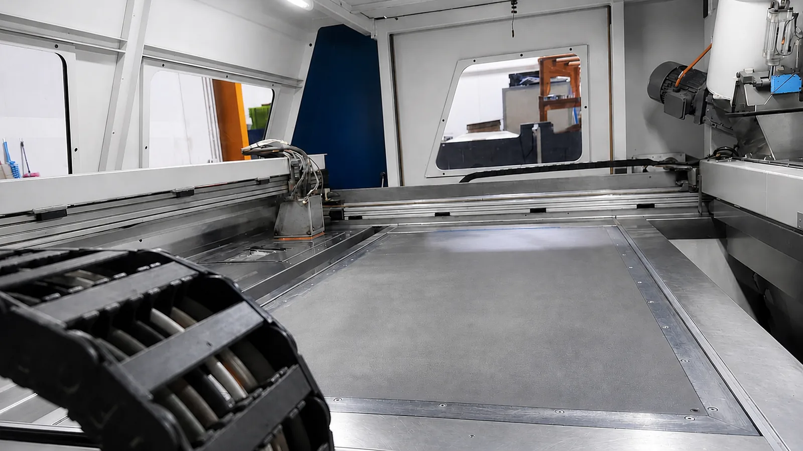 Interior of an industrial 3D sand printing machine showing the recoater rail and flat sand build area