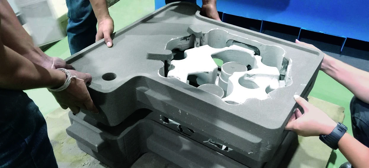Technicians lifting a 3D-printed sand mold section for a marine cylinder head casting